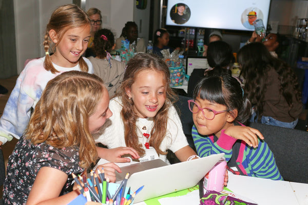 Children gathered around a table with a laptop, engaged in an activity.